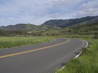 the bike is riding down the winding road between mountains, and a grassy valley in the background