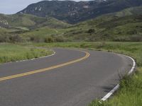 the bike is riding down the winding road between mountains, and a grassy valley in the background