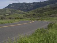 the bike is riding down the winding road between mountains, and a grassy valley in the background