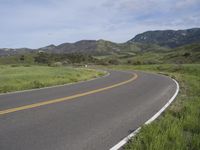 the bike is riding down the winding road between mountains, and a grassy valley in the background