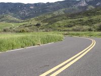 the bike is riding down the winding road between mountains, and a grassy valley in the background