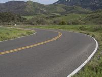 the bike is riding down the winding road between mountains, and a grassy valley in the background