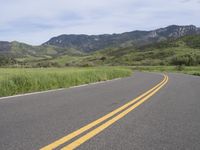 the bike is riding down the winding road between mountains, and a grassy valley in the background