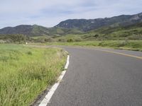 the bike is riding down the winding road between mountains, and a grassy valley in the background