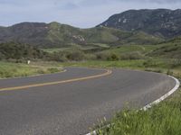 the bike is riding down the winding road between mountains, and a grassy valley in the background