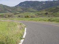 the bike is riding down the winding road between mountains, and a grassy valley in the background