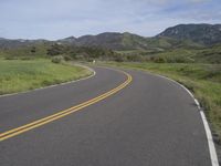 the bike is riding down the winding road between mountains, and a grassy valley in the background