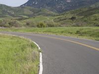 the bike is riding down the winding road between mountains, and a grassy valley in the background