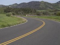 the bike is riding down the winding road between mountains, and a grassy valley in the background