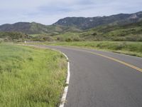 the bike is riding down the winding road between mountains, and a grassy valley in the background