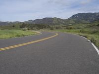 the bike is riding down the winding road between mountains, and a grassy valley in the background