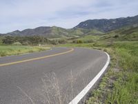 the bike is riding down the winding road between mountains, and a grassy valley in the background