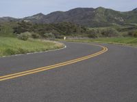 the bike is riding down the winding road between mountains, and a grassy valley in the background