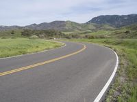 the bike is riding down the winding road between mountains, and a grassy valley in the background