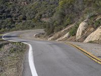 a motorcycle is on the road going uphill beside the hill and tree line that has a yellow strip in it