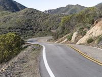 a motorcycle is on the road going uphill beside the hill and tree line that has a yellow strip in it