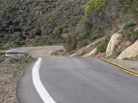 a motorcycle is on the road going uphill beside the hill and tree line that has a yellow strip in it