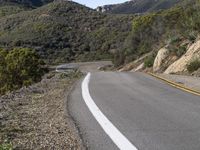 a motorcycle is on the road going uphill beside the hill and tree line that has a yellow strip in it