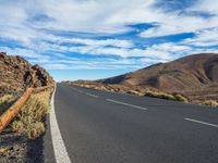 an empty road in a scenic area with mountains in the background and blue skies over them