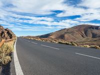 an empty road in a scenic area with mountains in the background and blue skies over them