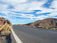 an empty road in a scenic area with mountains in the background and blue skies over them