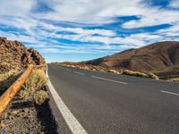 an empty road in a scenic area with mountains in the background and blue skies over them