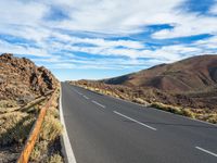 an empty road in a scenic area with mountains in the background and blue skies over them