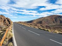 an empty road in a scenic area with mountains in the background and blue skies over them