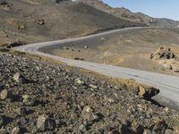 an empty road next to mountains with a small rock wall on one side and one end painted white