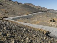 an empty road next to mountains with a small rock wall on one side and one end painted white