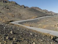 an empty road next to mountains with a small rock wall on one side and one end painted white