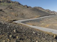 an empty road next to mountains with a small rock wall on one side and one end painted white