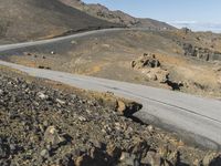 an empty road next to mountains with a small rock wall on one side and one end painted white