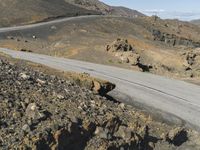 an empty road next to mountains with a small rock wall on one side and one end painted white