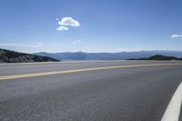 a long empty road with mountains and blue skies in the background, as seen from a vehicle