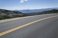 a long empty road with mountains and blue skies in the background, as seen from a vehicle