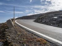 a paved road with a large curve and two street posts, against the backdrop of a mountainous hill