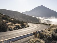 a curve in the middle of a road next to some mountains with steam coming from it