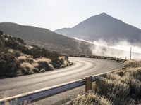 a curve in the middle of a road next to some mountains with steam coming from it