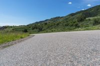 a paved road in the middle of some hills and grass with a few trees growing along the side