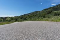 a paved road in the middle of some hills and grass with a few trees growing along the side