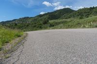 a paved road in the middle of some hills and grass with a few trees growing along the side