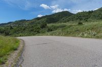 a paved road in the middle of some hills and grass with a few trees growing along the side