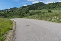 a paved road in the middle of some hills and grass with a few trees growing along the side