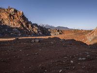 a red dirt road leading to a desert mountain with rocks and mountains in the background