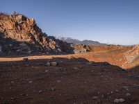 a red dirt road leading to a desert mountain with rocks and mountains in the background