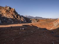 a red dirt road leading to a desert mountain with rocks and mountains in the background