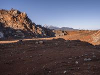 a red dirt road leading to a desert mountain with rocks and mountains in the background