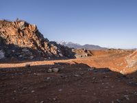 a red dirt road leading to a desert mountain with rocks and mountains in the background