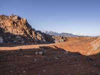 a red dirt road leading to a desert mountain with rocks and mountains in the background